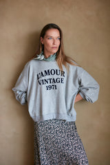 Model wears grey marle oversized sweater with logo
