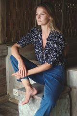 Woman sitting down wearing the Gigi jeans and a button front, puff sleeve shirt in a blue floral print.