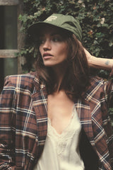 Woman wearing a green cap with logo and plaid jacket with a white top.