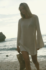 The Allegra Mesh Dress in Natural with flared sleeves worn as a beach throw on dress.