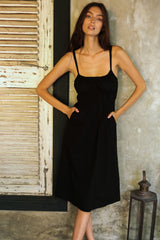 Model wears black cotton poplin midi dress with side pockets 