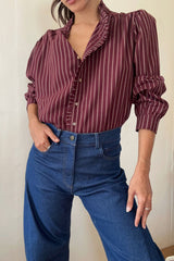 Model wears burgundy shirt in stripe print with frill detail