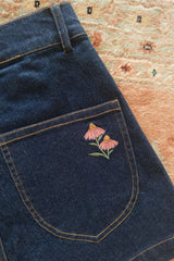 Close-up view of the tobacco stitch and embroidered flower detail on the denim shorts.