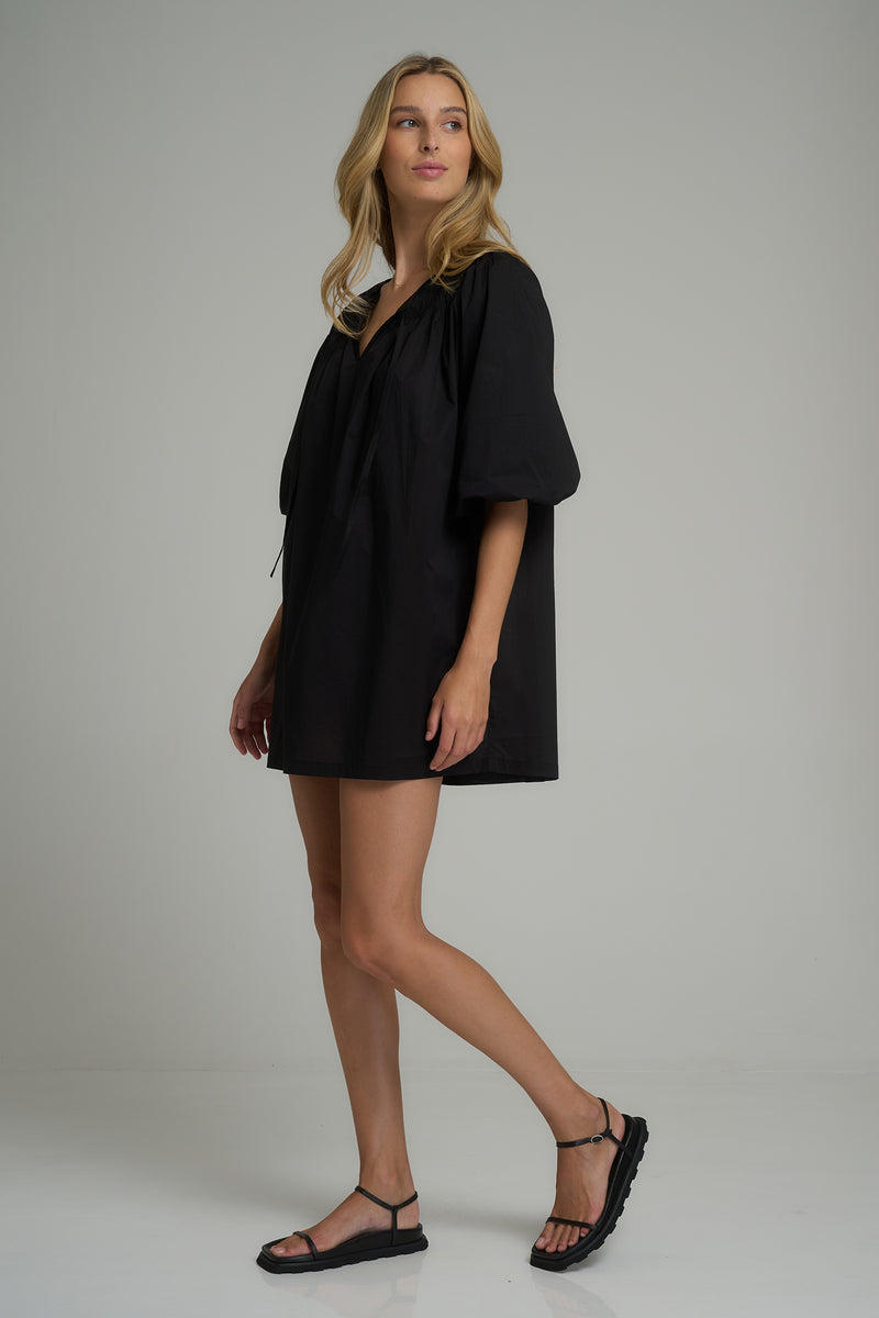 A woman wearing a black cotton mini dress with puff sleeves