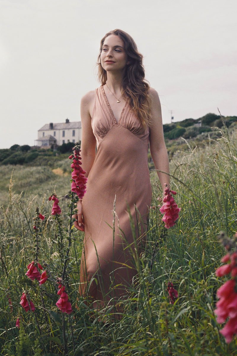 Woman in a beige dress standing in a field with pink flowers