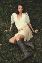Woman sitting on grass wearing a white cotton LILYA mini dress and black boots