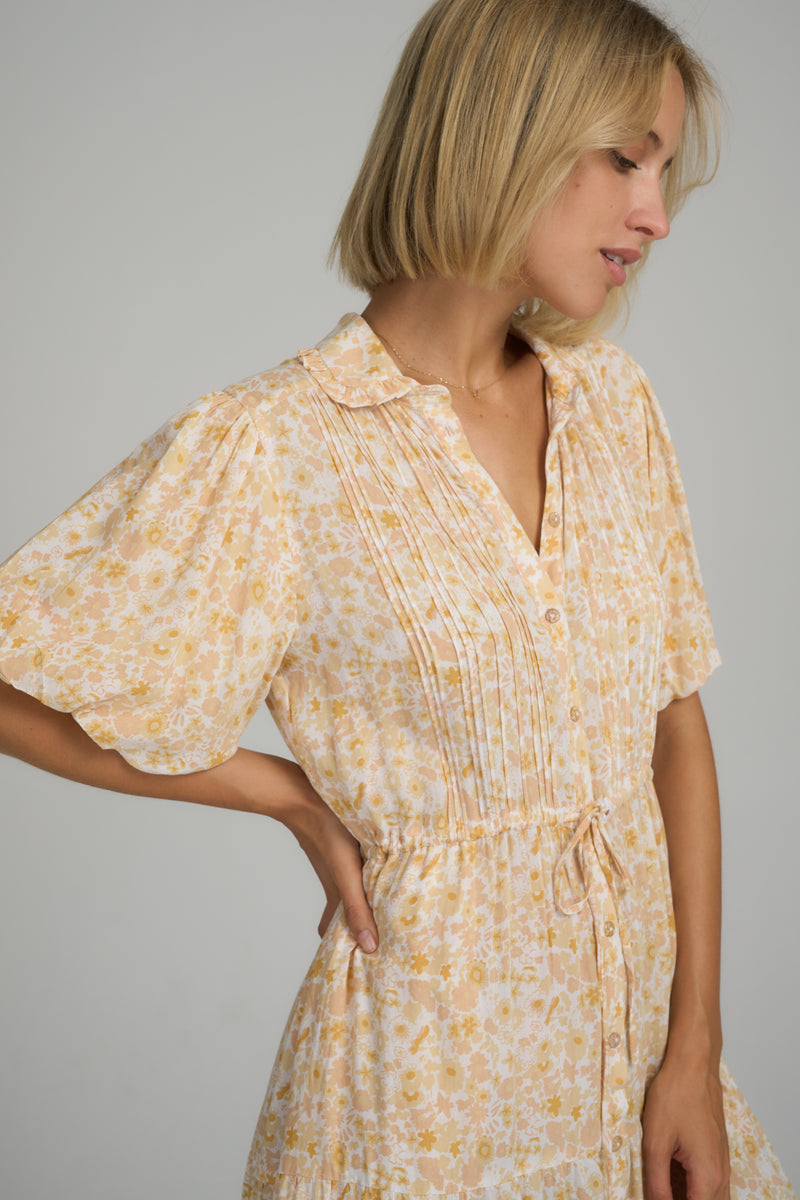 A woman wearing a yellow floral summer tea dress