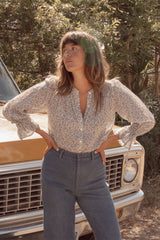 A woman wears the LILYA blouse with a button front lightly puffed sleeves and flared sleeve hem. 