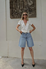 Woman wearing the white Monty Top by LILYA styled with denim shorts and heels