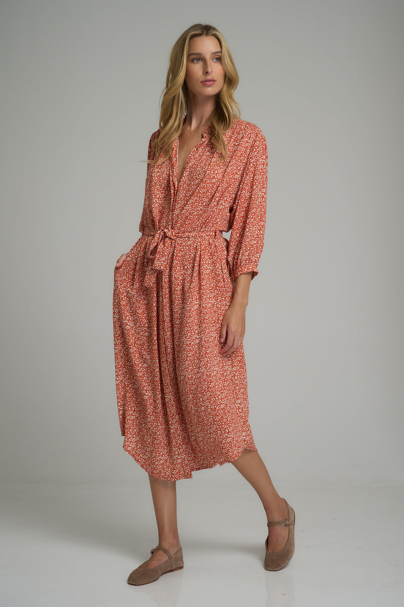 A woman wearing a orange and ivory floral dress with pockets