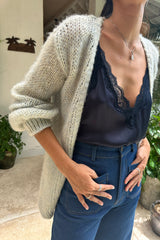 A woman wearing navy lace top, denim jeans and blue cardigan