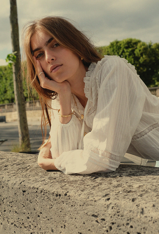 Woman in a white blouse sitting on a stone surface with trees in the background