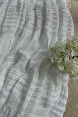 A close up of a white maxi dress with pleat details