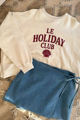 White sweatshirt with 'LE HOLIDAY CLUB' text and a chambray denim wrap skirt