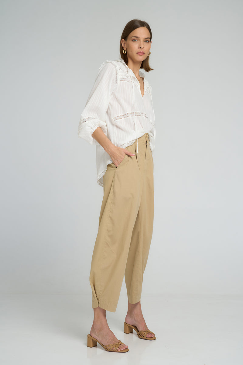 White cotton lace blouse with long sleeves and tie neckline paired with sand trousers