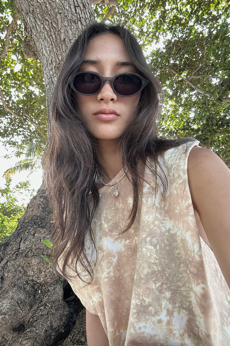 Woman wearing sunglasses and a sleeveless patterned top standing next to a tree