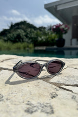 Sunglasses with pink lenses on a stone surface near a pool