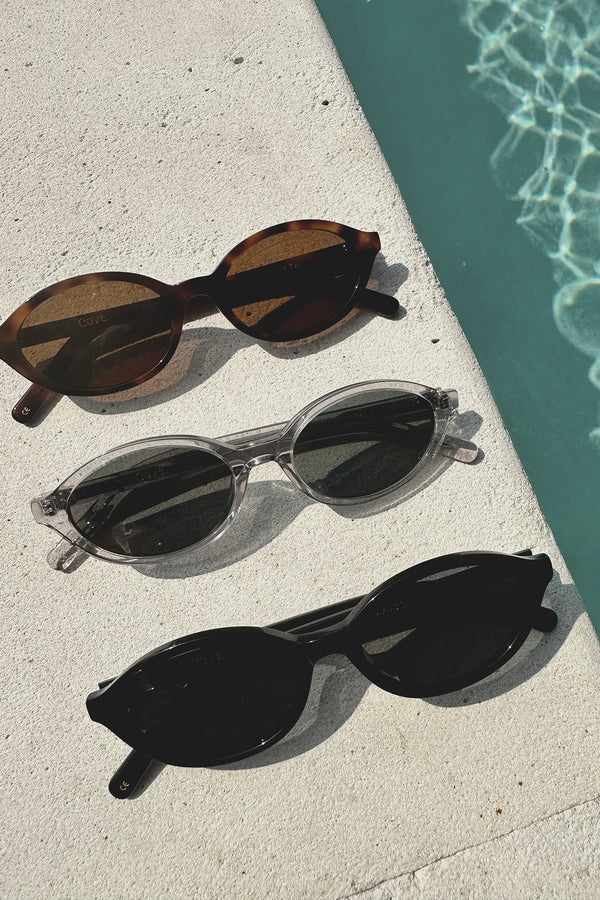 Three pairs of sunglasses on a concrete surface near a pool.