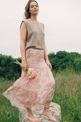 Woman in a sleeveless top and floral skirt standing in a field with greenery in the background