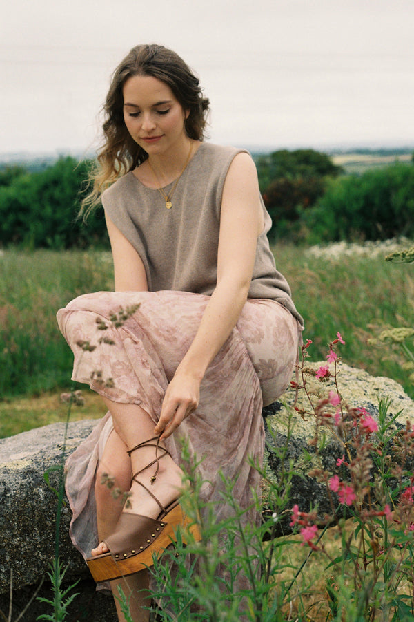 Woman sitting on a rock in a field with flowers wearing floral maxi skirt
