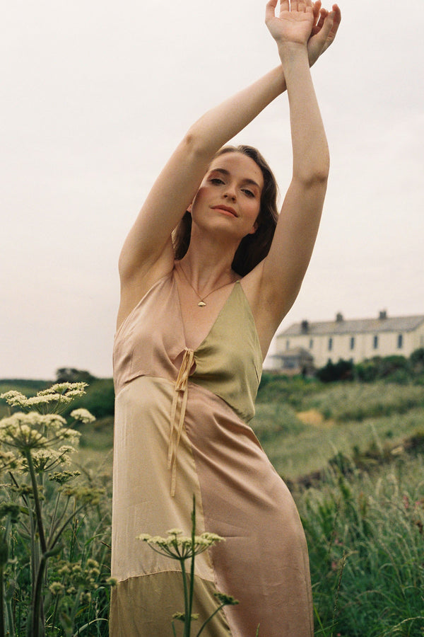 Woman in a layered dress standing in a field with a house in the background
