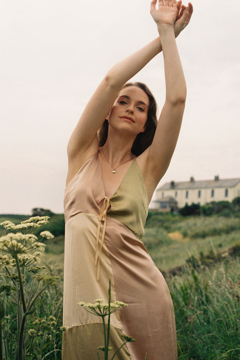 Woman in a layered dress standing in a field with a house in the background