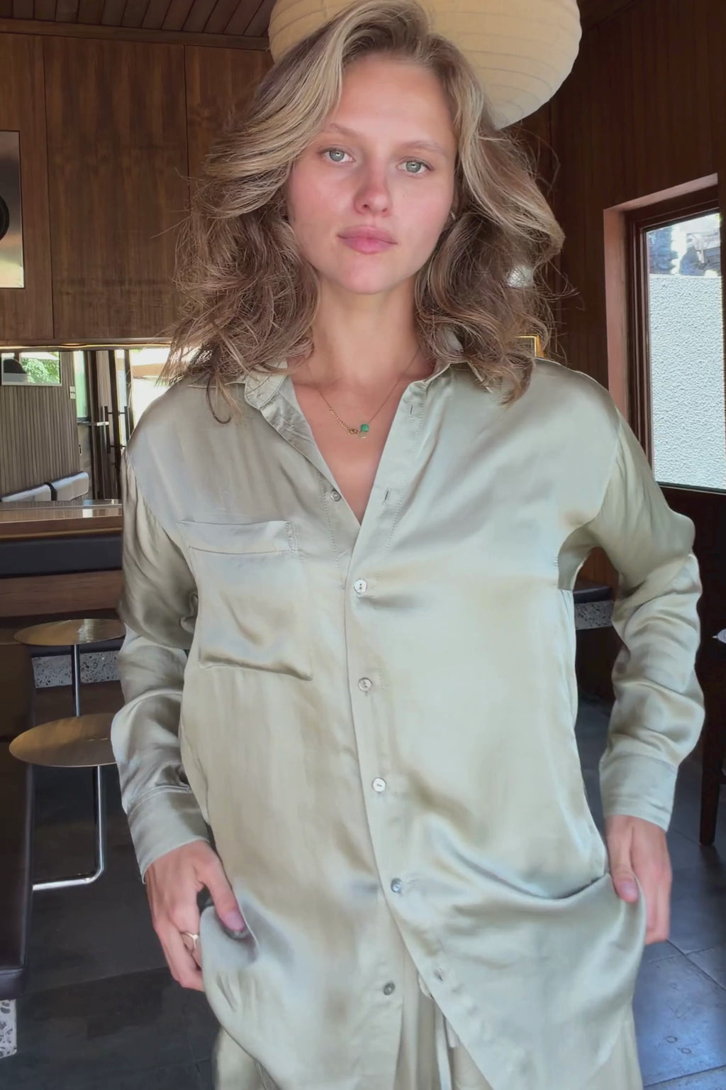 Model wears green satin shirt for summer with shell buttons and front pocket