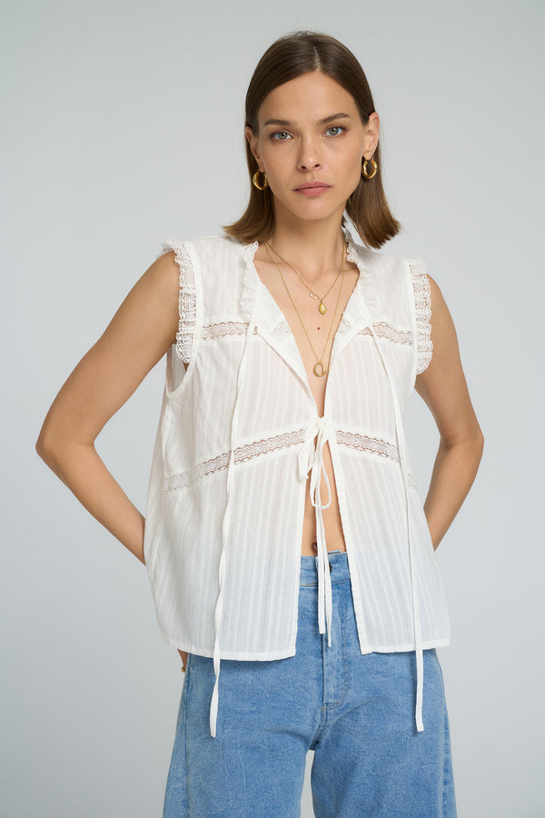 Model wearing LILYA Jupiter Lace Top in white cotton with lace trim details and tie front styling