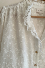 Detail photo of floral 
embroidery and lace trim on white blouse 